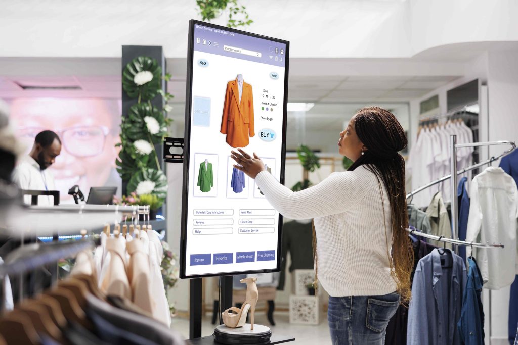 Woman buyer selecting clothes on board, using interactive touch screen monitor in clothing store